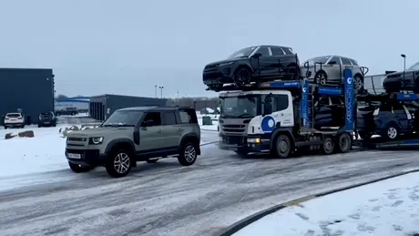 Un Land Rover Defender tractează un camion Scania care transportă șapte vehicule