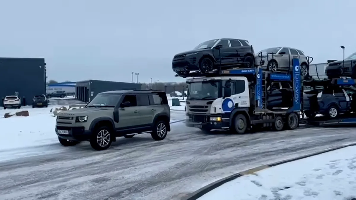 Un Land Rover Defender tractează un camion Scania care transportă șapte vehicule