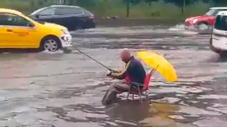 Bucureştean filmat vineri în timp ce ”pescuia” în mijlocul unei străzi inundate. Ce i-au urat şoferii - VIDEO